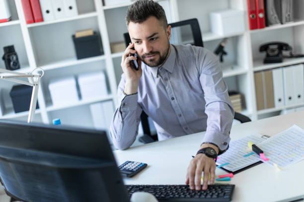 istock A young man is sitting in the office, talking on the phone and working on the computer. 960222948