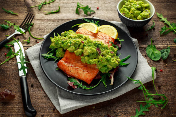 oven cooked salmon steak, fillet with avocado salsa and green on black plate. wooden table. healthy food - fruit sauce imagens e fotografias de stock