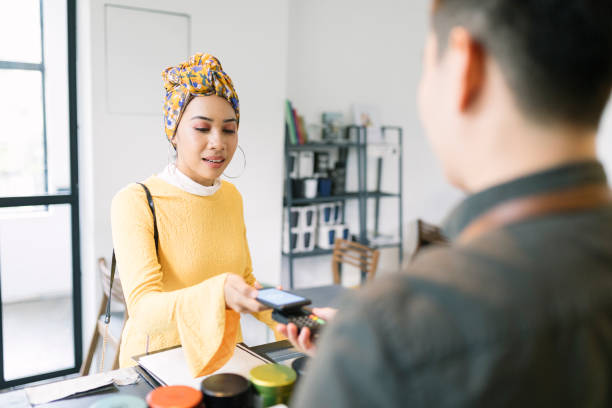 Young Woman Paying with Smartphone in a Cafe Young woman paying with smartphone using NFC technology. small business malaysia stock pictures, royalty-free photos & images