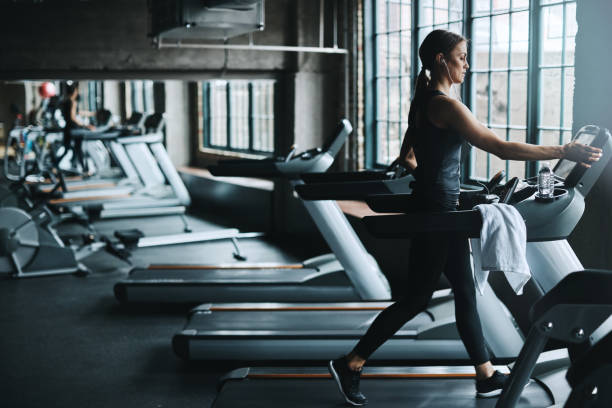 Using a machine to become one Shot of an attractive young woman working out on a treadmill in a gym treadmill photos stock pictures, royalty-free photos & images