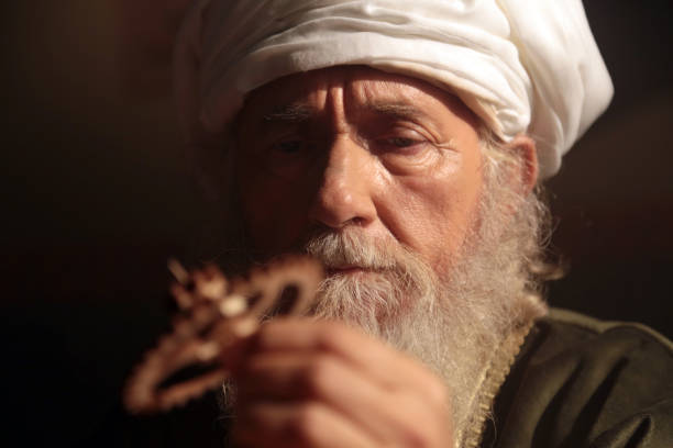 An old and historic Islamic scientist is working in his studio working on a wooden gear.