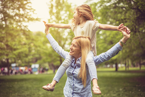 Mother carrying daughter on shoulders and spending time in park.