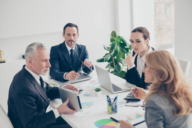 istock Handsome, aged, senior with grey hair showing presentation to his minded ponder colleagues using tablet, four business persons together sitting in work place, station at desk 960264128