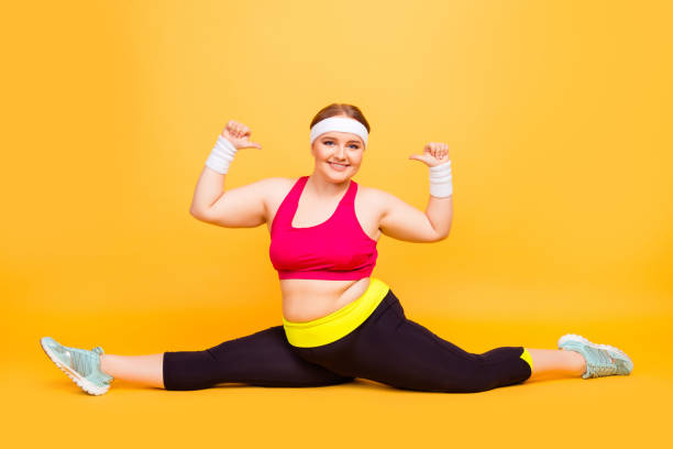 look at me i can do this! full-length image of excited cheerful joyful funny cute chubby woman doing splits on the floor and pointing on herself, isolated on yellow background - the splits ethnic women exercising imagens e fotografias de stock