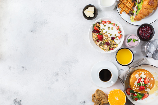 Food and drink, healthy morning eating concept. Breakfast assortment with pancakes, waffles, croissant sandwich and granola with yogurt on the table. Top view flat lay copy space background