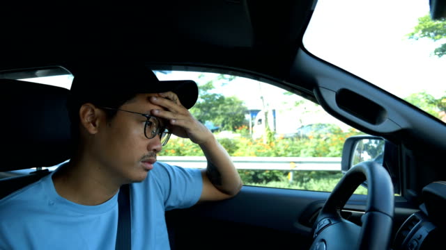 Young boring Asian man driving a car on traffic jam.