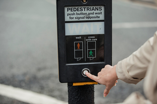 Unrecognisable female young adult pressing the button to use the pedestrian crossing.