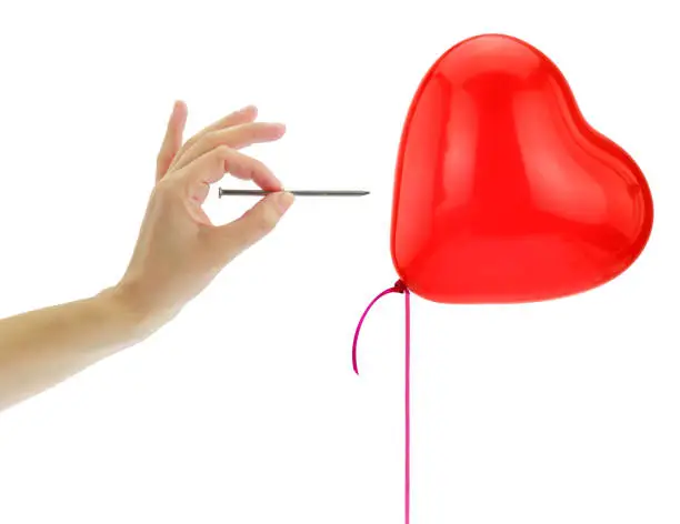 Nail about to pop a heart balloon isolated on white