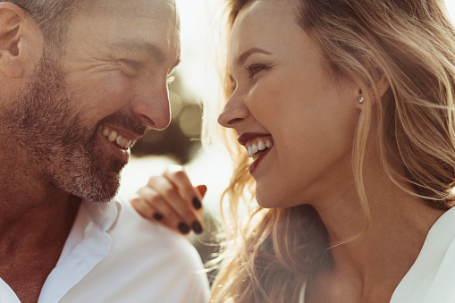 Close up of cheerful man and woman outdoors. Romantic couple together looking at each other and smiling.