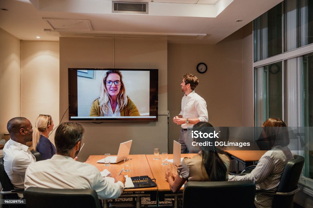 Late Night Video Conference Meeting Group of business people having a late night video conference meeting. Sitting around a conference table talking and networking. Video Conference Stock Photo