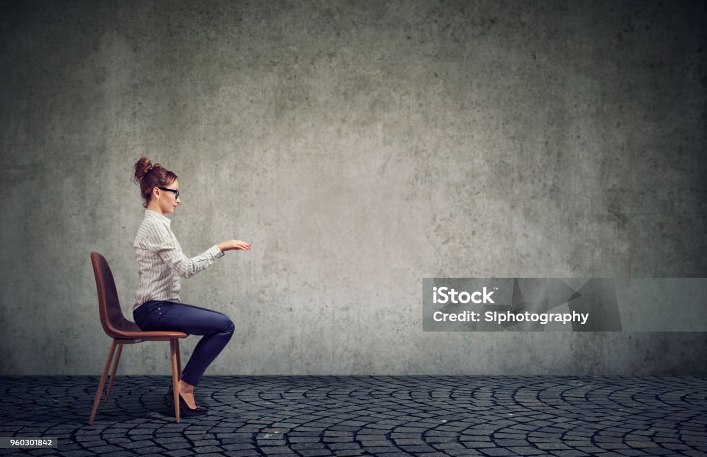 Woman sitting at imaginary table Side view of an employee woman in glasses sitting at invisible table pretending to type on computer. Sitting Stock Photo