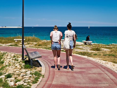 Monopoli,Italy,16/05/2018; two girls a sunny morning to the Monopoli territory,that walking on the pathway of the park of the beach.