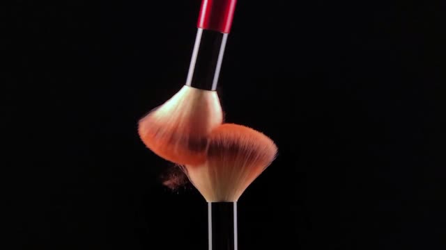 Slow motion of Two make-up brush spreading on black background.