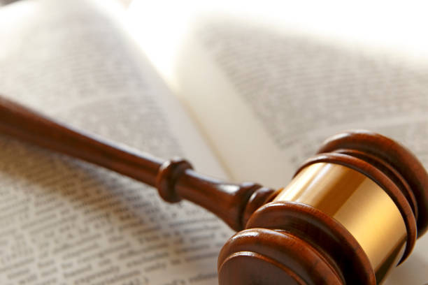 A wooden gavel rests on top of an open law book as the late afternoon sun shines through a window and casts the gavels shadow across the book.