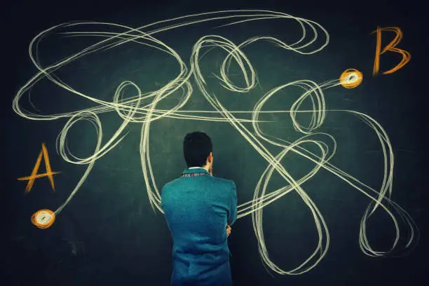 Rear view of a puzzled businessman in front of a blackboard finding the correct way from point A to point B. Solving problem, find solution, business idea and creativity concept.