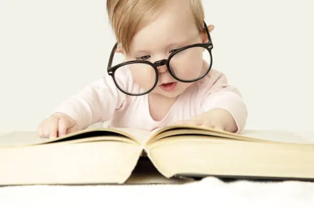 Photo of Adorable baby in front of big thick book, studio shot