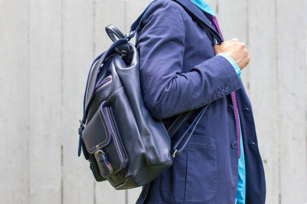 Casual wear detail: stylish man in blue suit with leather backpack. White wooden background.