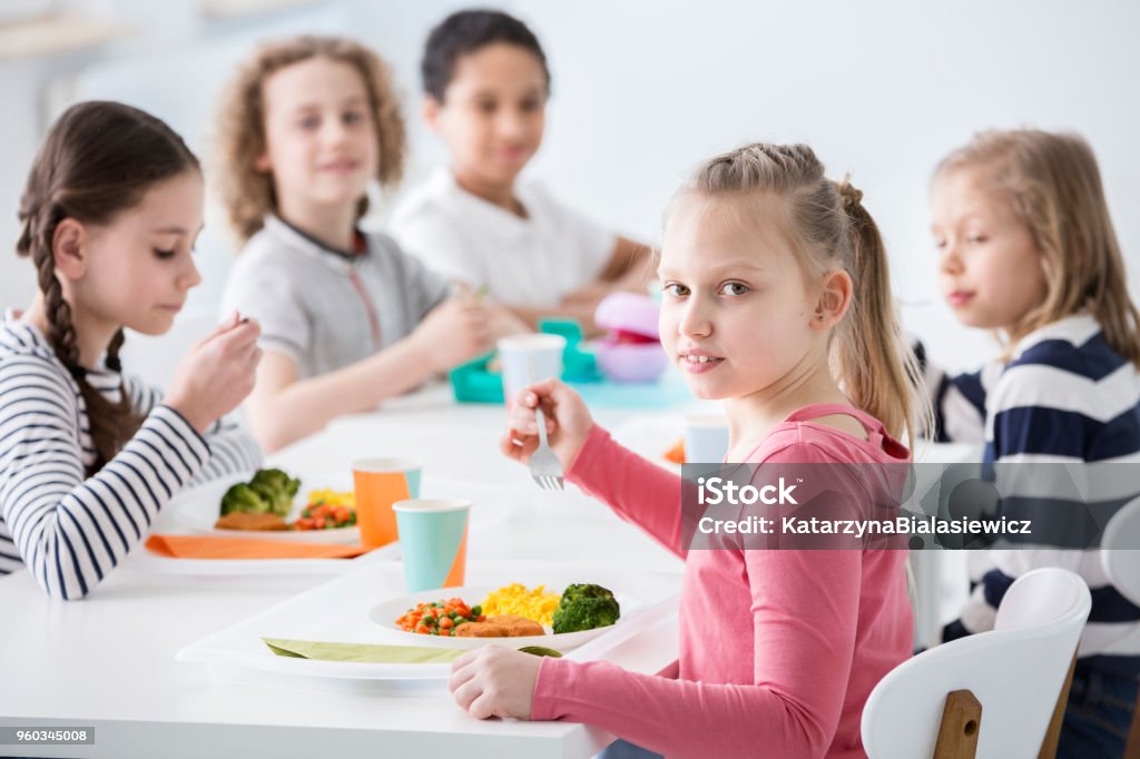 Fille, manger des légumes avec des amis à la cantine pendant la pause à l’école - Photo de Cantine libre de droits
