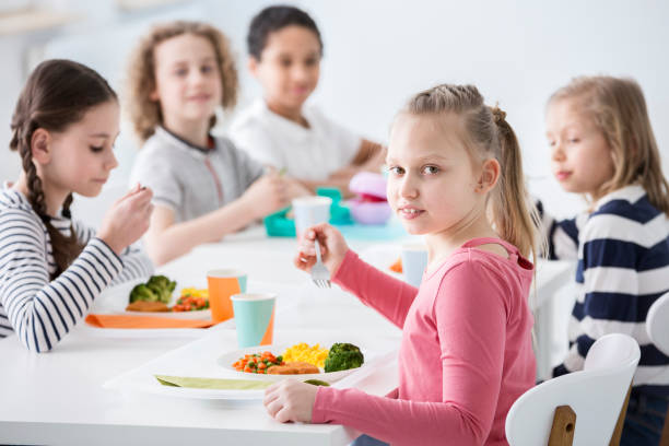 girl eating vegetables with friends in the canteen during break at school - child food school children eating imagens e fotografias de stock