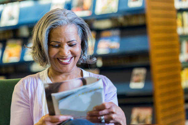 istock Happy senior woman reading magazine in library 960388550