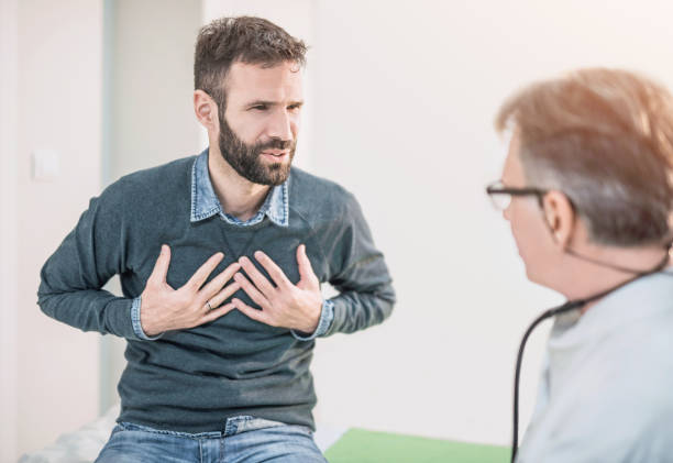 mitte erwachsenen männlichen patienten beschreiben einen schmerz in der brust zu seinem arzt. - asthmatisch stock-fotos und bilder