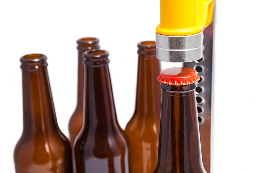 Bottle capper with many bottles of beer isolated on white