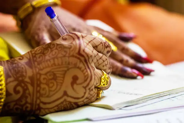 a newly married indian bengali wife with golden wedding ring signing marriage registration form