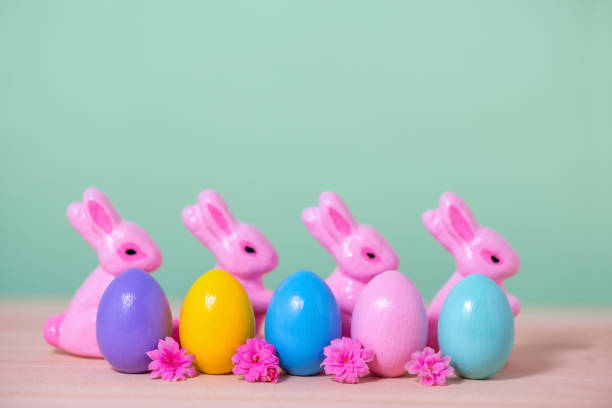 istock row multi colored painted Easter eggs, pink Bunnies and flowers over green background, holiday background 960440682