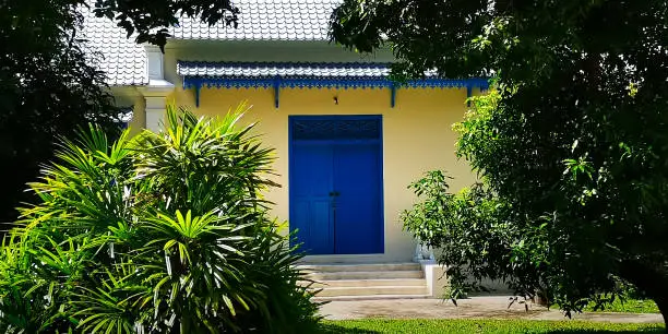 And old, yet stunning, newly painted, blue double-door, on a classic beautiful Thai structure, with a lovely green garden and walkway for visitors and functions, off of a main street in Bangkok, Thailand.