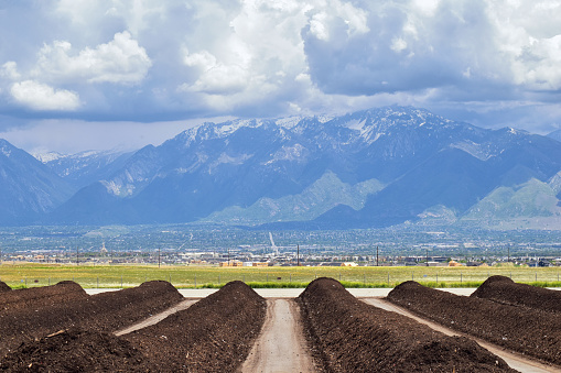 Rows of Compost ready for sale with Panoramic view of Wasatch Front Rocky Mountains, Great Salt Lake Valley in early spring with melting snow and Cloudscape. Utah. USA.