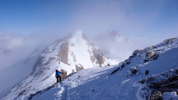 mężczyzna narciarz backcountry wędrówki do wysokiego alpejskiego szczytu w szwajcarii wzdłuż grzbietu skalnego i śniegu w lekkiej mgle - silvretta zdjęcia i obrazy z banku zdjęć