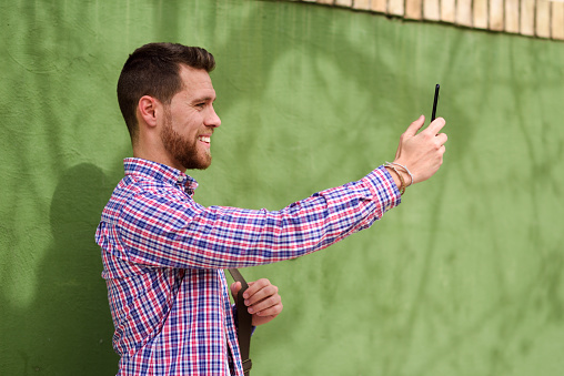 Young man taking photographs with his smart phone in urban background. Guy wearing casual clothes. Lifestyle concept.
