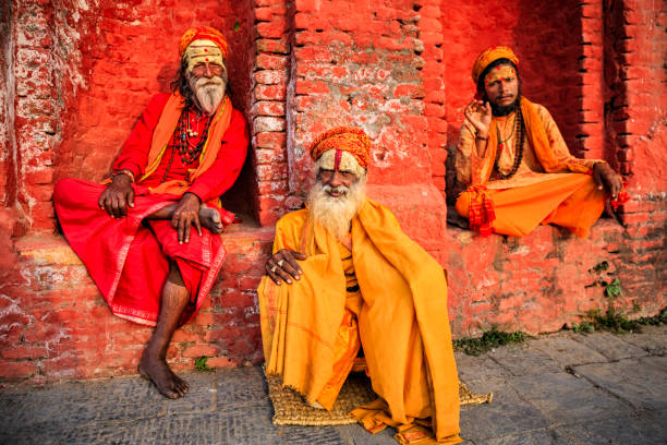 Sadhu - indian holymen sitting in the temple In Hinduism, sadhu, or shadhu is a common term for a mystic, an ascetic, practitioner of yoga (yogi) and/or wandering monks. The sadhu is solely dedicated to achieving the fourth and final Hindu goal of life, moksha (liberation), through meditation and contemplation of Brahman. Sadhus often wear ochre-colored clothing, symbolizing renunciation. varanasi photos stock pictures, royalty-free photos & images