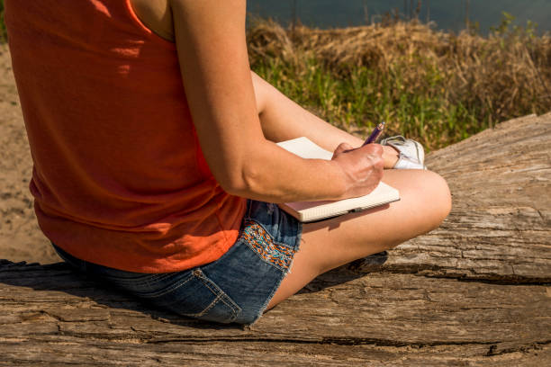 istock young woman sitting on tree trunk and writing in her diary 960480996