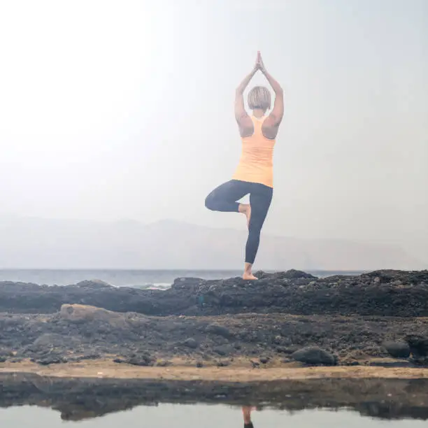 Woman meditating in yoga pose, ocean view, beach and rocks. Motivation and inspirational summer sea landscape, healthy lifestyle concept.