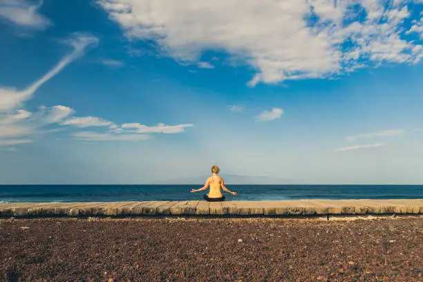 Woman meditating in yoga pose, ocean view, beach and wooden sidewalk. Motivation and inspirational summer sea landscape. Healthy lifestyle outdoors in nature concept.