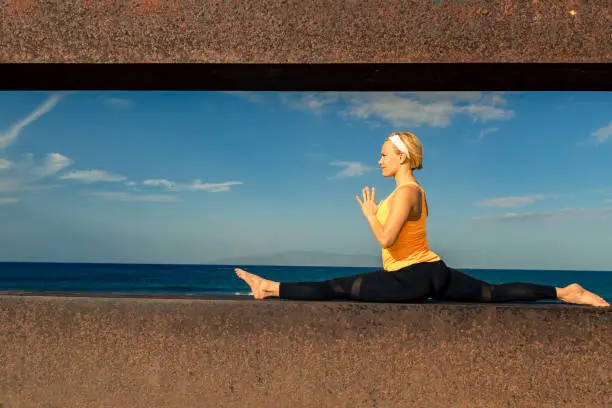 Woman meditating in yoga pose, ocean view, beach and wooden sidewalk. Motivation and inspirational summer sea landscape. Healthy lifestyle outdoors in nature concept.