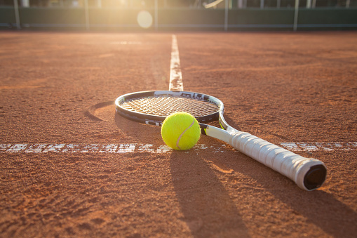 Close-up tennis racket and ball placed on court ground.