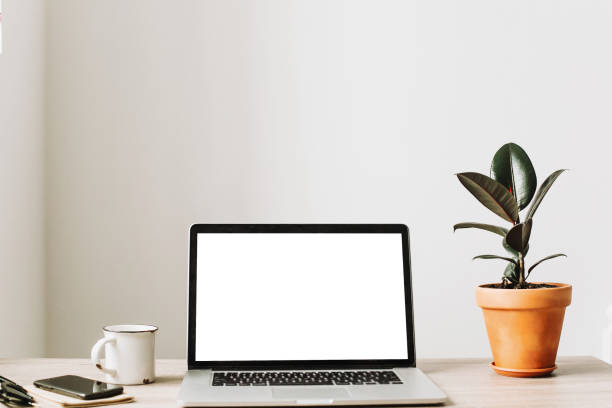 istock Laptop with empty screen on wooden desktop with phone, notebook, coffee and plant. space for text. mock-up. business workspace. working online home. Freelance concept. 960516494