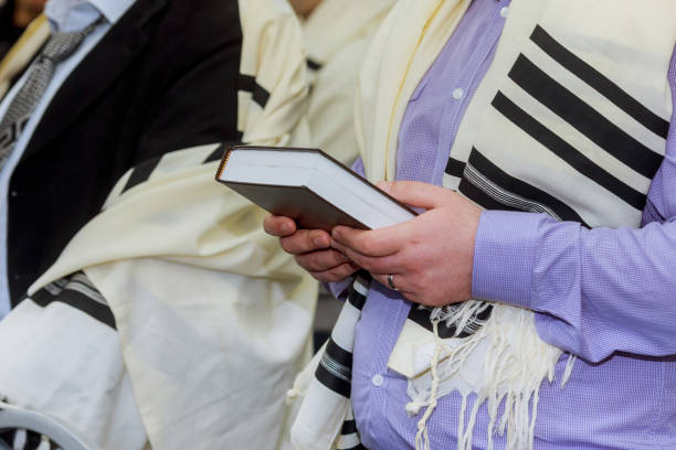 mani in possesso di un libro di preghiere ebraico che indossa uno scialle da preghiera - synagogue foto e immagini stock