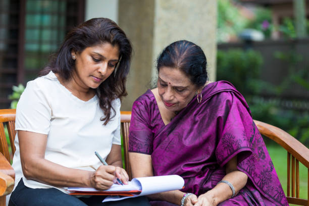 que se inclina en el papel como la hija llena la última algunas secciones del documento. - malaysian person family asian ethnicity mother fotografías e imágenes de stock