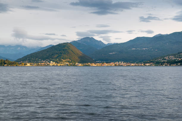 lago maggiore, italien. piemont ufer mit den städten von intra und verbania im morgengrauen, beleuchtet von der sonne durch die wolken. blick vom ufer laveno. im hintergrund die alpen - intra coastal stock-fotos und bilder