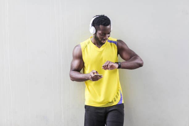 istock dark skinned sporty man holding smartphone and looking smart watch 960560000