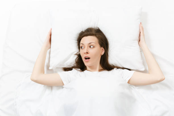 Top view of head of tired brunette young woman lying in bed with white sheet, pillow, blanket. Shocked pretty female spending time in room. Rest, relax, good mood concept. Copy space advertisement vista superior de la cabeza de mujer joven morena cansada tumbada en la cama con sábana blanca, almohada, manta. sorprendió bastante femenino pasar tiempo en la habitación. descansar, relajarse, concepto de buen humor. copiar espacio para anuncio