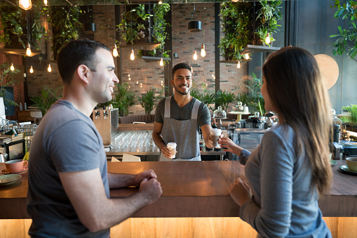 Waiter serving coffee to go to a happy couple at a cafe on the bar counter - food service occupation concepts