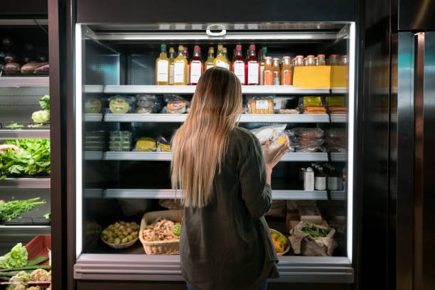 Woman buying food at the supermarket Woman buying food at the supermarket and reading a label on a product - lifestyle concepts refrigerated section supermarket photos stock pictures, royalty-free photos & images