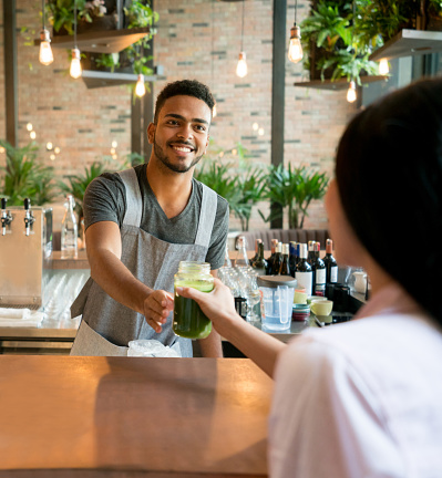 Happy waiter serving drinks to a customer at a cafe on the bar counter - food service occupation concepts