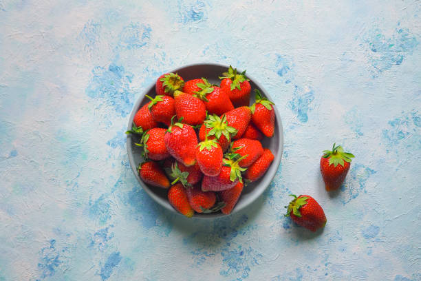 A plate with ripe strawberries on a blue table.