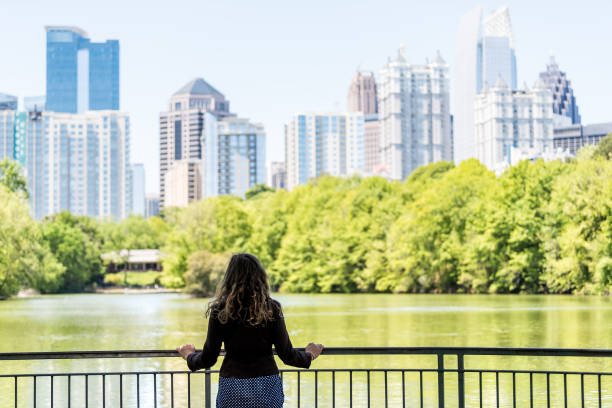 giovane donna in piedi nel piedmont park di atlanta, georgia guardando l'acqua panoramica e lo skyline del paesaggio urbano dei grattacieli urbani del centro, lago clara meer - piedmont park foto e immagini stock