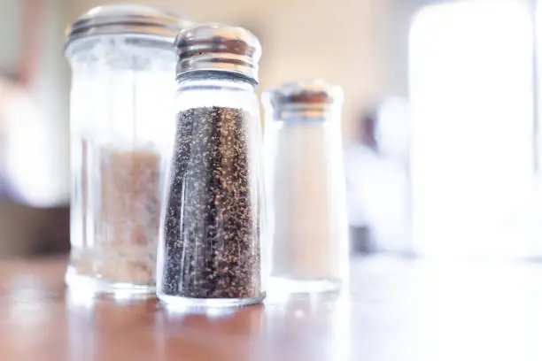 Macro closeup of salt, pepper and brown raw sugar shakers in bottles on wooden table in rustic restaurant